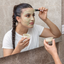 Woman brushing on a Katari Argil green clay masque in the mirror
