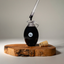 Dropper of thick Katari black castor oil over a hand-blown glass amphora on an olivewood board