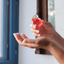 Hands pouring Katari Granate pomegranate seed oil by a blue Mediterranean window