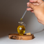 Dropper of Katari Hoba pure jojoba oil over a hand-blown glass amphora on an olivewood board