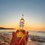 Hand holding Katari Amour d'été perfume oil against a Mediterranean beach sunset