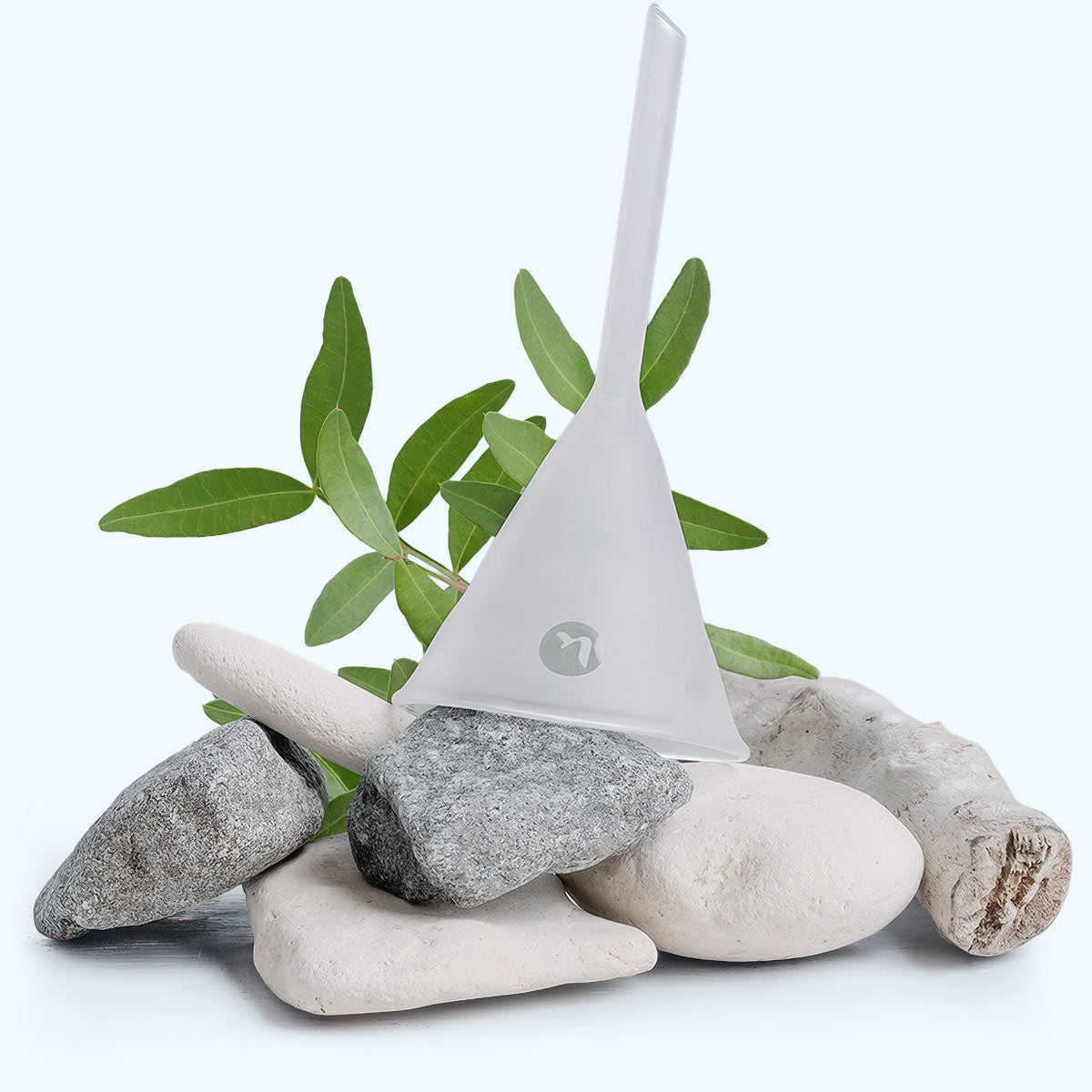 a frosted hand blown funnel set on top of grey and white pebbles and driftwood on a light background