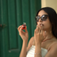 Woman in sunglasses smelling Katari Granate pomegranate seed oil in front of a green door
