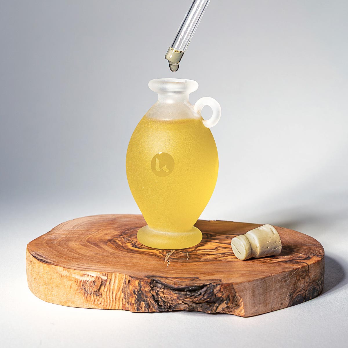 Dropper applying Katari Barie — Prickly Pear Cactus Seed Oil into a frosted glass amphora on a natural wood slice.