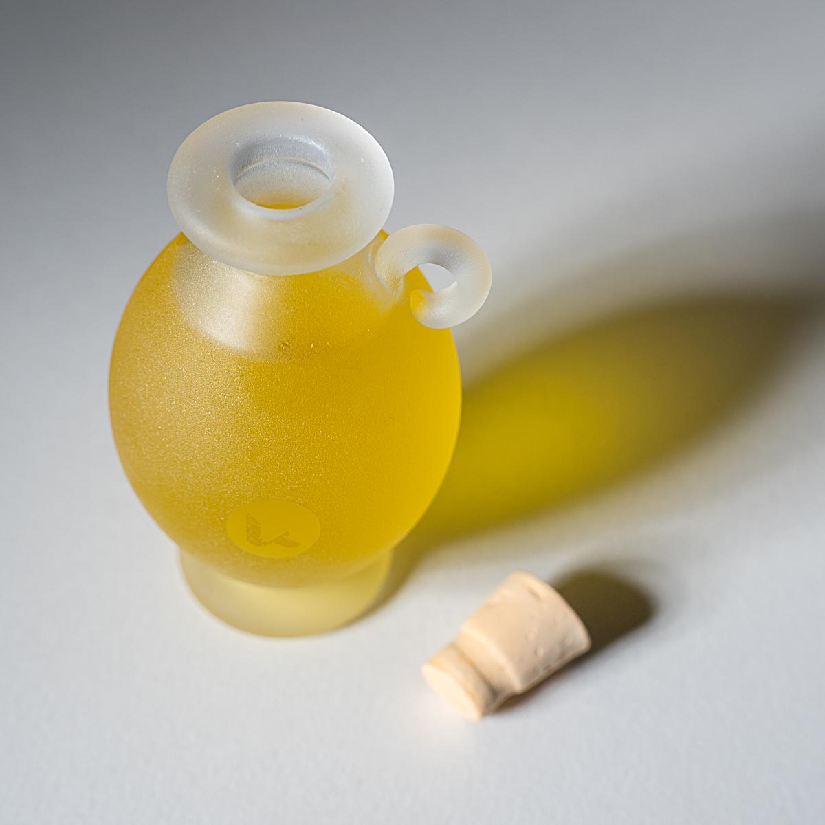 Top view of Katari Barie — Prickly Pear Cactus Seed Oil in a frosted glass amphora with a cork stopper on a white surface.