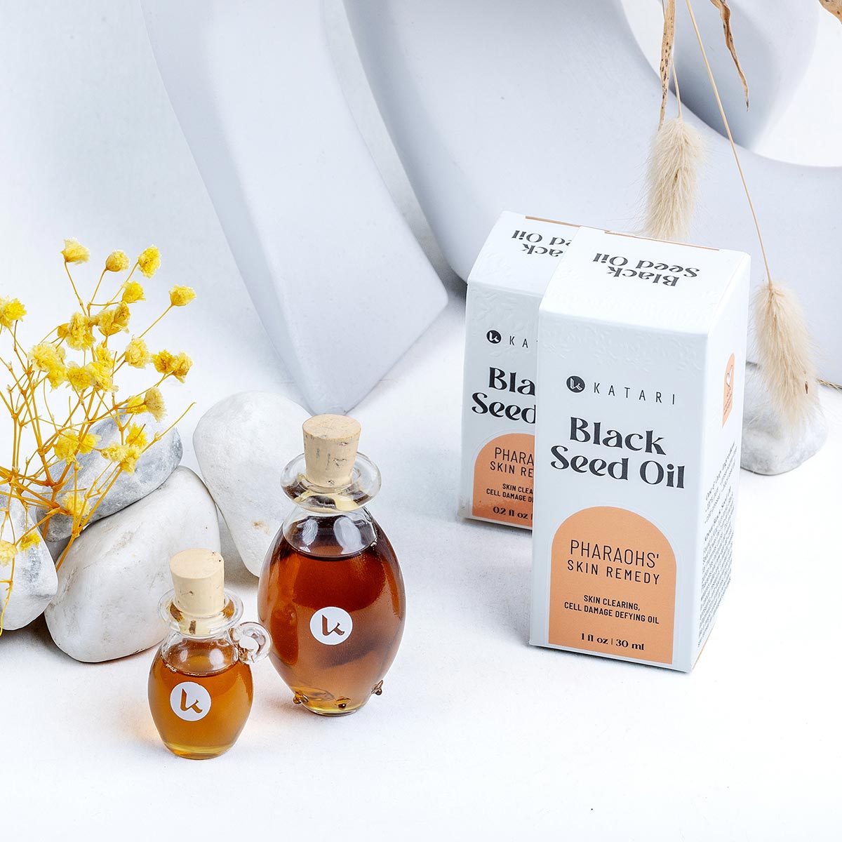 Katari Black Seed Oil in two hand-blown glass amphoras with its retail box, a pure cold-pressed thymoquinone (TQ) source for skin clearing.