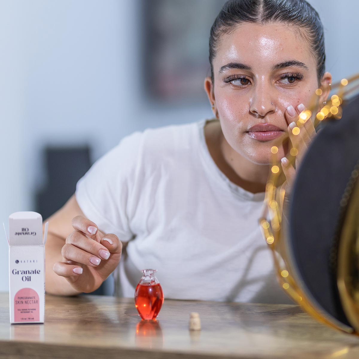 Woman applying Katari Granate Oil, a 100% pure cold-pressed pomegranate seed oil, from a small hand-blown glass amphora during her skincare routine.