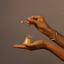 Hands scooping Katari Poudre de Barie exfoliating powder from a hand-blown glass jar with a glass spoon