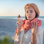 Woman in a turban and coral scarf holding Katari Roseau rose water toner on a Tunisian beach at sunset