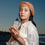 Woman in a turban holding Katari Roseau rose water toner on the beach at dusk