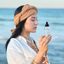 Woman by the sea holding a frosted bottle of Katari Roseau rose water