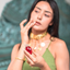 Woman in a gold necklace holding a hand-blown glass amphora of Katari Rubi rosehip oil